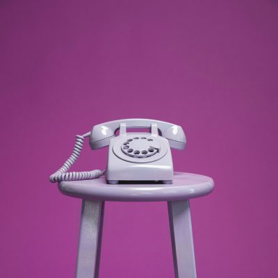 Photo d'un téléphone à cadran sur un tabouret, le tout sur fond violet.